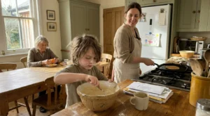A grandmother, mother, and child preparing breakfast together in a sunlit, authentic kitchen, illustrating a family tradition.