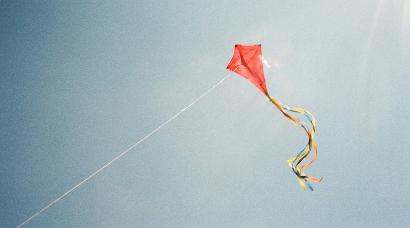 A red kite flying in a blue sky, with its string representing the balance between structure and flexibility.